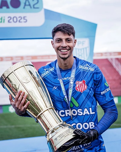 "Goleiro Guilherme Nogueira sorri enquanto segura o troféu de campeão da Série A2 Paulista de 2025, vestindo uniforme azul do Capivariano após a conquista."