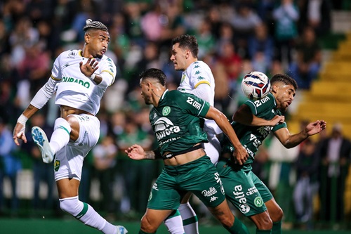 Derik Lacerda, atacante do Cuiabá, salta para finalizar a jogada em meio à marcação da Chapecoense, em partida pela Série B na Arena Condá.