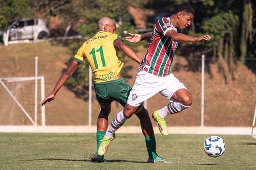 "Jogadores do Cuiabá e do Fluminense disputam a bola durante partida de futebol em campo aberto, com gramado verde e gol ao fundo."