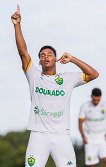 Jogador do Cuiabá Sub-20 comemora gol com o dedo apontado para o céu durante partida do Campeonato Brasileiro Sub-20, vestindo uniforme branco com escudo do Dourado.