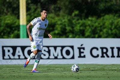 Jogador do Cuiabá Sub-20 conduz a bola durante partida no CT, com faixa "Racismo é Crime" ao fundo.
