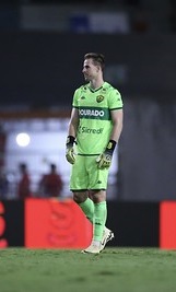 Goleiro Pasinato em campo com uniforme verde neon do Cuiabá, durante partida da Série B, após importante defesa contra o CRB.