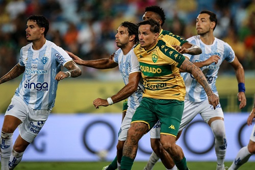 Jogadores do Cuiabá e Paysandu disputam espaço dentro da área durante uma partida intensa de futebol, com destaque para a marcação acirrada e o uniforme amarelo e verde do Cuiabá.