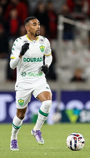 O lateral Matheusinho, do Cuiabá, em ação durante um jogo, vestindo o uniforme branco com detalhes verde e amarelo. Ele corre no gramado, conduzindo a bola com a perna direita em direção ao ataque.