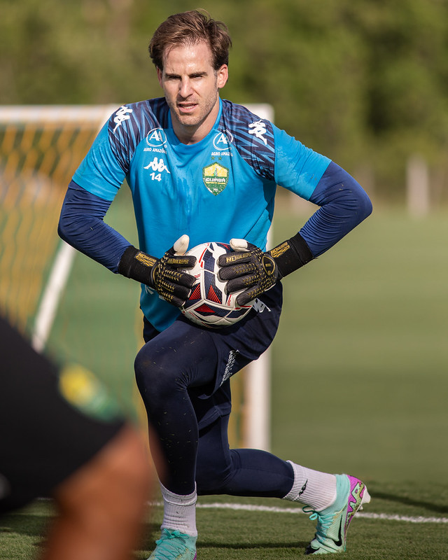 “Goleiro do Cuiabá EC realizando treino com bola no CT, usando luvas e uniforme azul, em preparação física antes dos próximos jogos da temporada.”