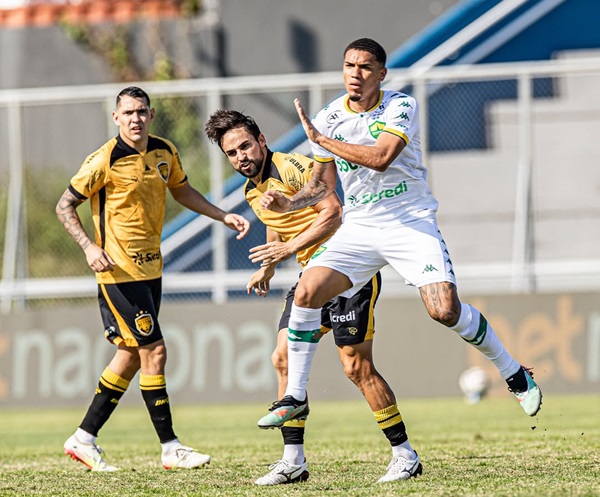 Jogadores do Cuiabá e do Amazonas disputam lance durante a partida pela Série B no estádio Carlos Zamith. O atleta do Cuiabá, com uniforme branco e detalhes verdes, avança em velocidade sob o forte sol de Manaus.