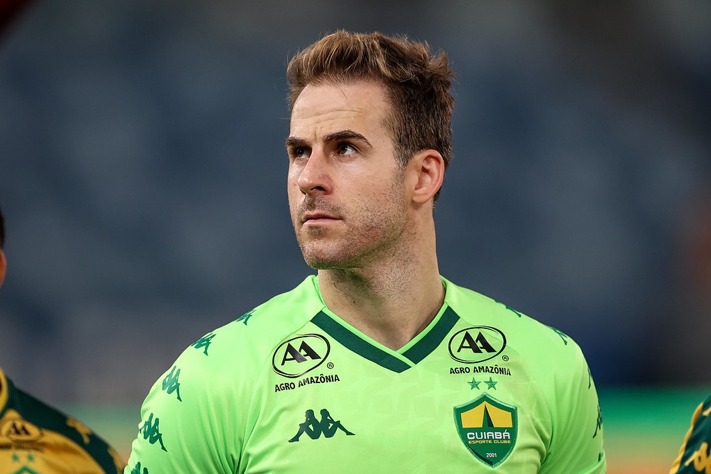 “Jogador do Cuiabá Esporte Clube durante atividade de treinamento, segurando a bola com firmeza, com uniforme azul e luvas de goleiro, em campo de treino ao ar livre.”