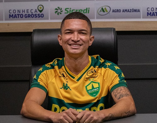 Jogador Marlon do Cuiabá EC sentado à mesa de coletiva, sorrindo, usando uniforme oficial do clube com patrocinadores visíveis ao fundo.