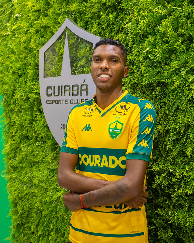 Vinícius Peixoto com a camisa do Cuiabá Esporte Clube ao lado do escudo oficial no CT Manoel Dresch.