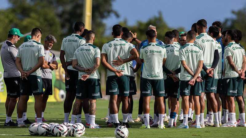 Elenco do Cuiabá reunido em treino no CT, jogadores em círculo ouvindo orientações da comissão técnica antes de confronto contra o Gama