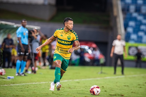 Jadson do Cuiabá em partida oficial conduz a bola no campo durante jogo noturno, vestindo uniforme verde e amarelo do Dourado.