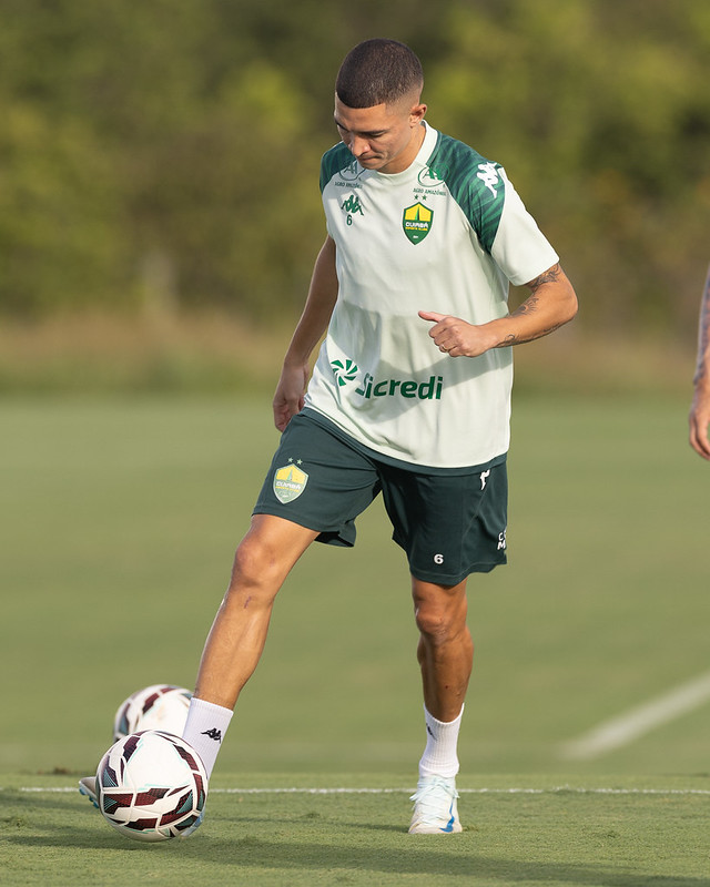 Lateral Marlon do Cuiabá Esporte Clube, vestindo o uniforme de treino verde claro e calções verde-escuros da marca Kappa, foca no controle de bola durante uma atividade no gramado. O logotipo da Sicredi está em destaque na camisa e o escudo do clube é visível no peito e no calção.