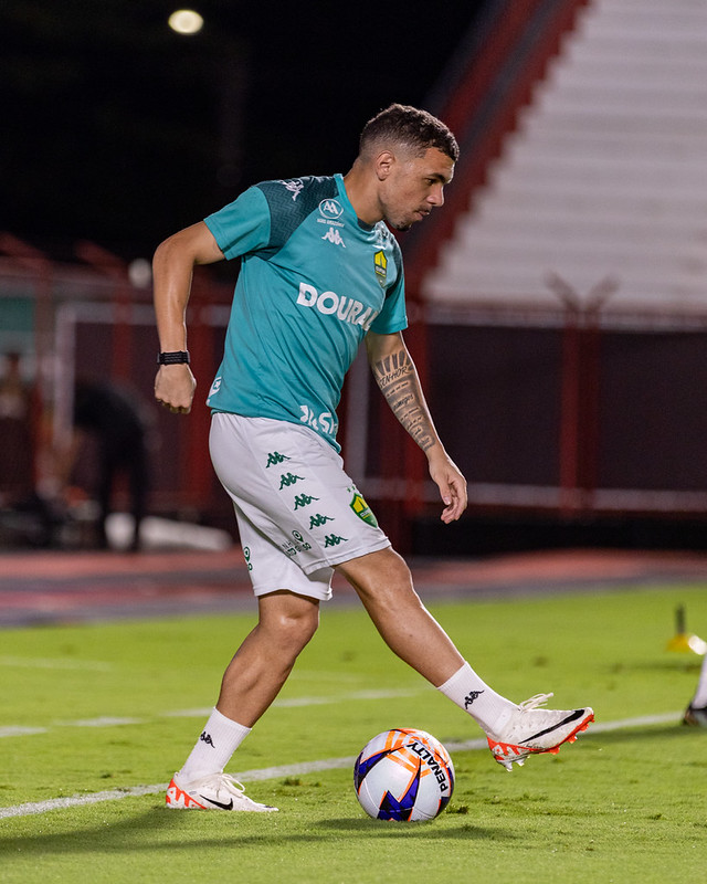 Um jogador com o uniforme alternativo/de treino na cor verde-água praticando controle de bola. Ele está usando uma bola da marca Penalty , uma fornecedora comum de bolas para torneios regionais brasileiros.