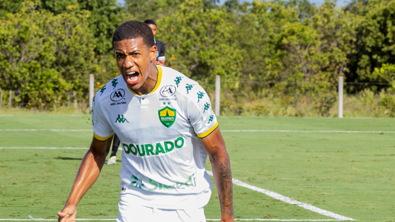 Atleta do Cuiabá Esporte Clube Sub-20 comemora com grito de emoção durante partida, vestindo uniforme branco e verde, destacando intensidade e competitividade do jogo.