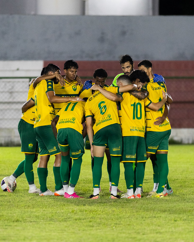 Jogadores do Cuiabá reunidos em roda no campo antes da partida, usando uniforme amarelo e verde, demonstrando união e concentração durante jogo da Copa Centro-Oeste.