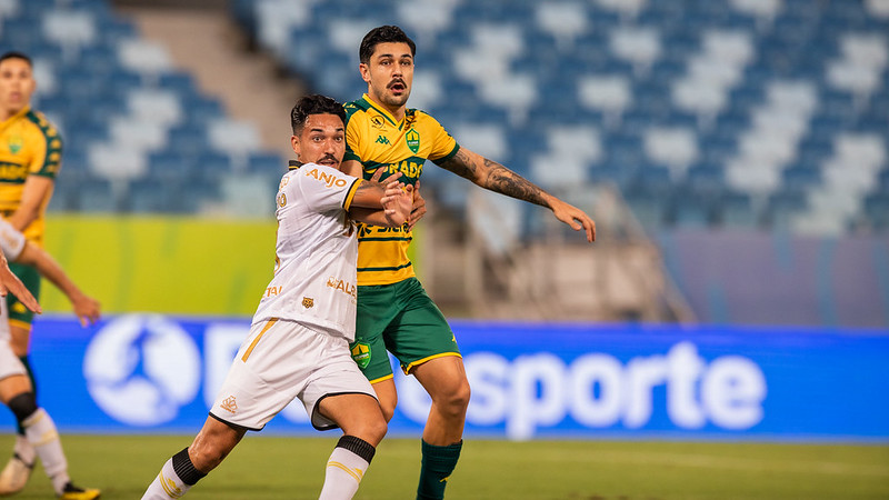 Jogador do Cuiabá Esporte Clube disputa bola com atleta do Criciúma Esporte Clube durante partida na Arena Pantanal, em lance intenso pelo Campeonato Brasileiro Série B.