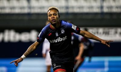 Ele é retratado em ação durante sua passagem pelo futebol grego, vestindo o uniforme do A.E. Kifisia. A foto captura um momento de comemoração ou foco intenso durante uma partida da Super Liga Grega.