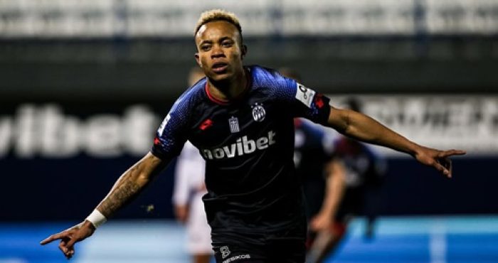 Ele é retratado em ação durante sua passagem pelo futebol grego, vestindo o uniforme do A.E. Kifisia. A foto captura um momento de comemoração ou foco intenso durante uma partida da Super Liga Grega.