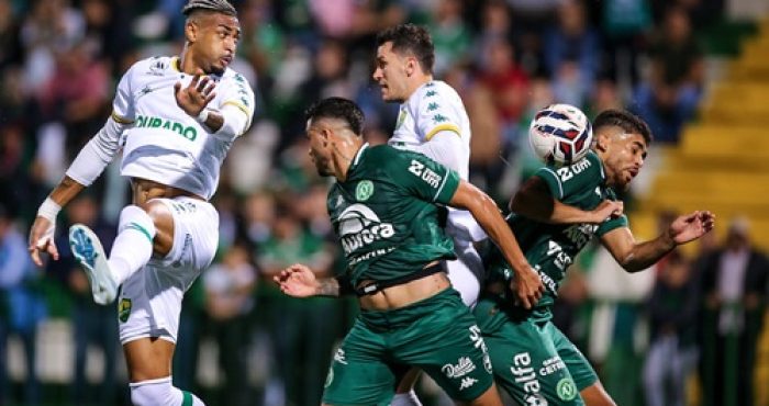 Derik Lacerda, atacante do Cuiabá, salta para finalizar a jogada em meio à marcação da Chapecoense, em partida pela Série B na Arena Condá.