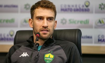 "Alan Empereur, zagueiro e capitão do Cuiabá, em coletiva de imprensa usando agasalho oficial do clube e falando ao microfone."