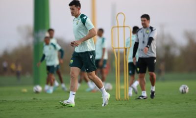 “Jogador do Cuiabá participando de atividade com bola no campo de treino, cones e boneco de treinamento ao fundo, acompanhado pela comissão técnica.”