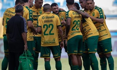 O time do Cuiabá reunido no centro do campo, possivelmente em uma roda de conversa antes ou durante o jogo.