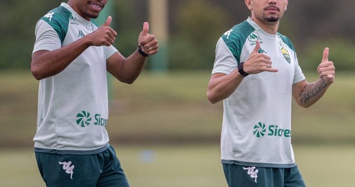 Dois jogadores do Cuiabá Esporte Clube durante treino no CT, vestindo uniforme branco e verde, fazendo sinal positivo com as mãos antes da estreia no Campeonato Mato-grossense.
