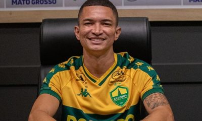 Jogador Marlon do Cuiabá EC sentado à mesa de coletiva, sorrindo, usando uniforme oficial do clube com patrocinadores visíveis ao fundo.