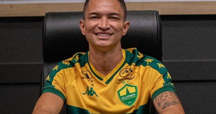 Jogador Marlon do Cuiabá EC sentado à mesa de coletiva, sorrindo, usando uniforme oficial do clube com patrocinadores visíveis ao fundo.