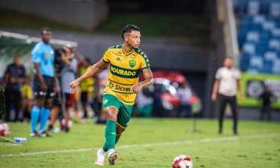 Jadson do Cuiabá em partida oficial conduz a bola no campo durante jogo noturno, vestindo uniforme verde e amarelo do Dourado.