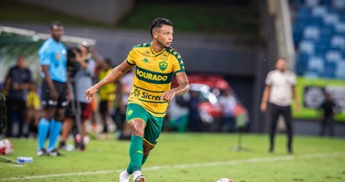 Jadson do Cuiabá em partida oficial conduz a bola no campo durante jogo noturno, vestindo uniforme verde e amarelo do Dourado.