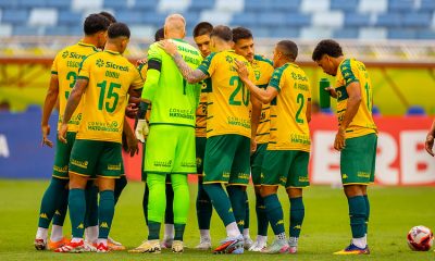 Jogadores do Cuiabá EC reunidos em círculo antes da partida na Arena Pantanal, usando uniforme amarelo e verde, em jogo do Campeonato Mato-grossense.