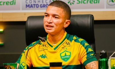 Close do jogador Marlon em uma coletiva de imprensa. Ele tem pele clara, cabelo raspado e uma tatuagem visível no braço esquerdo. Veste a camisa de treino amarela do clube e está posicionado em frente a um microfone, com uma expressão focada enquanto fala.