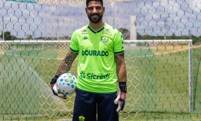 Marcelo Carné, goleiro do Cuiabá, posa no gramado em frente à rede do gol com uniforme verde e bola nas mãos.