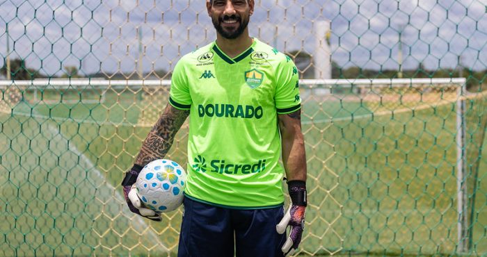Marcelo Carné, goleiro do Cuiabá, posa no gramado em frente à rede do gol com uniforme verde e bola nas mãos.