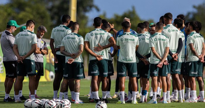Elenco do Cuiabá reunido em treino no CT, jogadores em círculo ouvindo orientações da comissão técnica antes de confronto contra o Gama