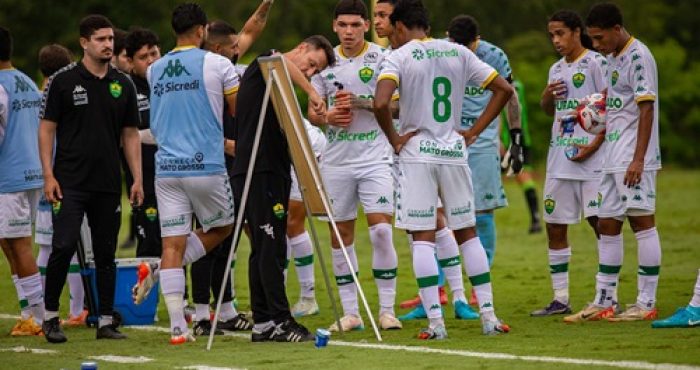 Jogadores do Cuiabá reunidos em treino no campo, com comissão técnica orientando taticamente a equipe.