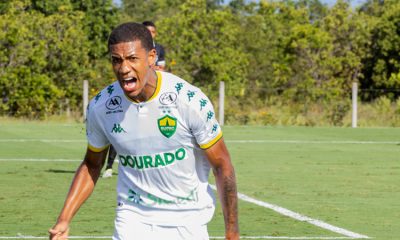 Atleta do Cuiabá Esporte Clube Sub-20 comemora com grito de emoção durante partida, vestindo uniforme branco e verde, destacando intensidade e competitividade do jogo.