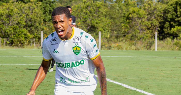 Atleta do Cuiabá Esporte Clube Sub-20 comemora com grito de emoção durante partida, vestindo uniforme branco e verde, destacando intensidade e competitividade do jogo.