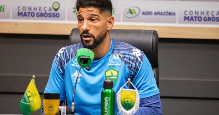 Marcelo Carné durante entrevista coletiva do Cuiabá Esporte Clube, falando ao microfone em sala de imprensa, com backdrop de patrocinadores ao fundo.