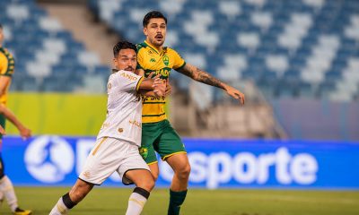Jogador do Cuiabá Esporte Clube disputa bola com atleta do Criciúma Esporte Clube durante partida na Arena Pantanal, em lance intenso pelo Campeonato Brasileiro Série B.