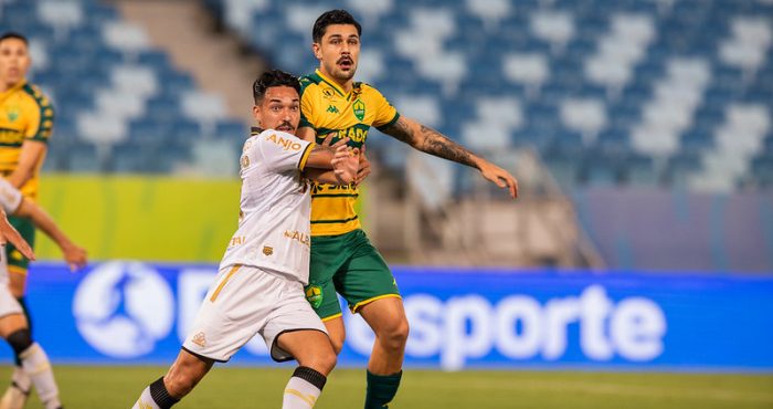 Jogador do Cuiabá Esporte Clube disputa bola com atleta do Criciúma Esporte Clube durante partida na Arena Pantanal, em lance intenso pelo Campeonato Brasileiro Série B.