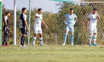 “Jogadores das categorias de base do Cuiabá EC posicionados na área durante partida contra o Corinthians em campo de treinamento, com uniforme branco do Dourado e rede do gol ao fundo.”