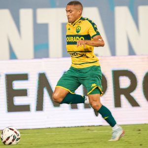 Jogador do Cuiabá EC conduz a bola durante partida na Arena Pantanal, vestindo uniforme amarelo e verde do Dourado em lance ofensivo contra o Novorizontino pela Série B.
