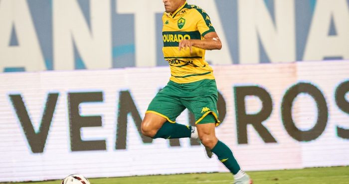 Jogador do Cuiabá EC conduz a bola durante partida na Arena Pantanal, vestindo uniforme amarelo e verde do Dourado em lance ofensivo contra o Novorizontino pela Série B.