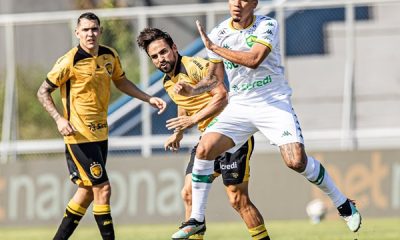 Jogadores do Cuiabá e do Amazonas disputam lance durante a partida pela Série B no estádio Carlos Zamith. O atleta do Cuiabá, com uniforme branco e detalhes verdes, avança em velocidade sob o forte sol de Manaus.