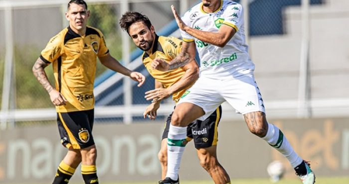 Jogadores do Cuiabá e do Amazonas disputam lance durante a partida pela Série B no estádio Carlos Zamith. O atleta do Cuiabá, com uniforme branco e detalhes verdes, avança em velocidade sob o forte sol de Manaus.