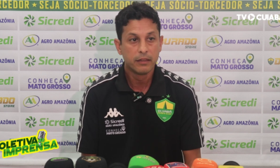auxiliar técnico Gustavo Almeida concede entrevista coletiva após jogo do Cuiabá, sentado à mesa com microfone e bandeira do clube ao fundo com patrocinadores.