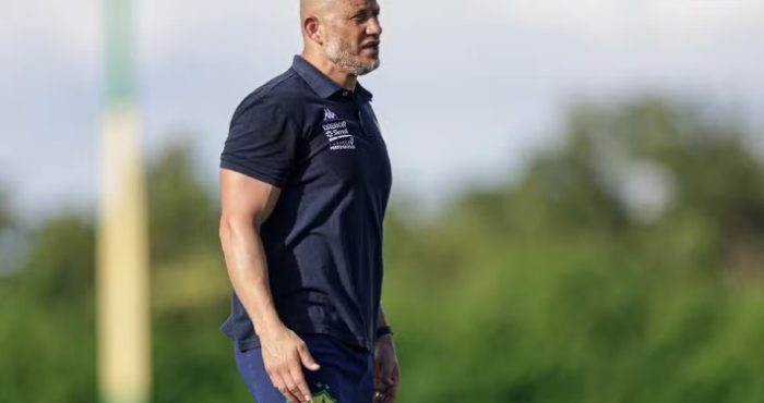 Treinador do Cuiabá durante atividade no campo, usando uniforme azul, com expressão séria enquanto observa o treino da equipe.