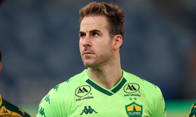 “Jogador do Cuiabá Esporte Clube durante atividade de treinamento, segurando a bola com firmeza, com uniforme azul e luvas de goleiro, em campo de treino ao ar livre.”